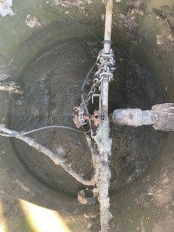 Top-down view of a dirty circular well with pipes and tangled wires inside