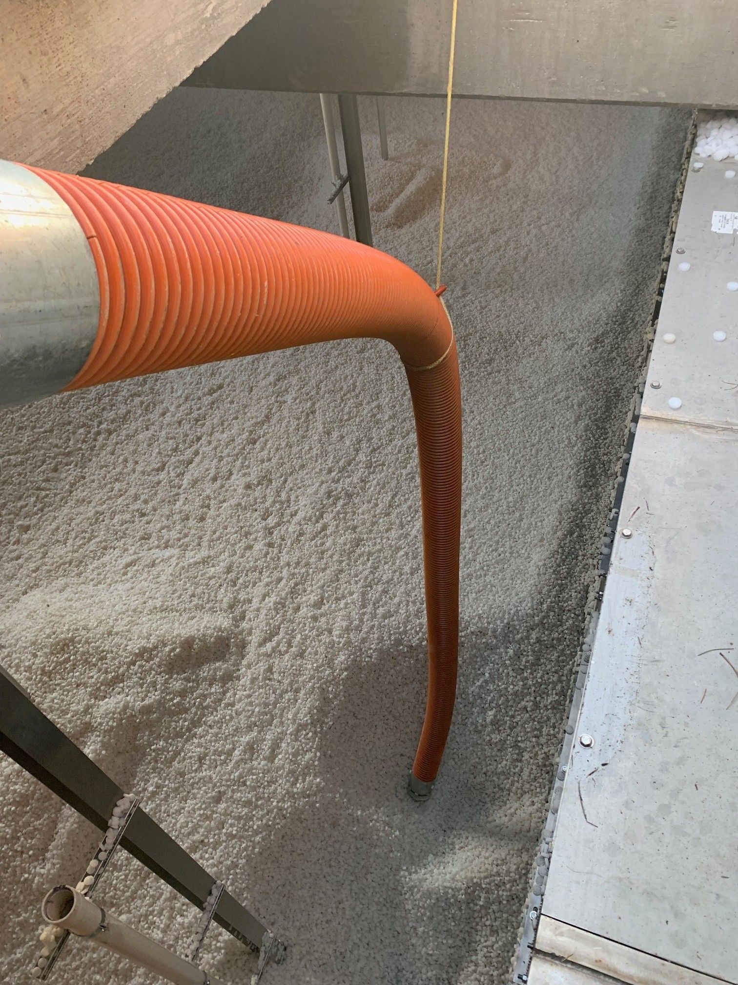 Orange flexible hose draining liquid into a concrete trench or basin.