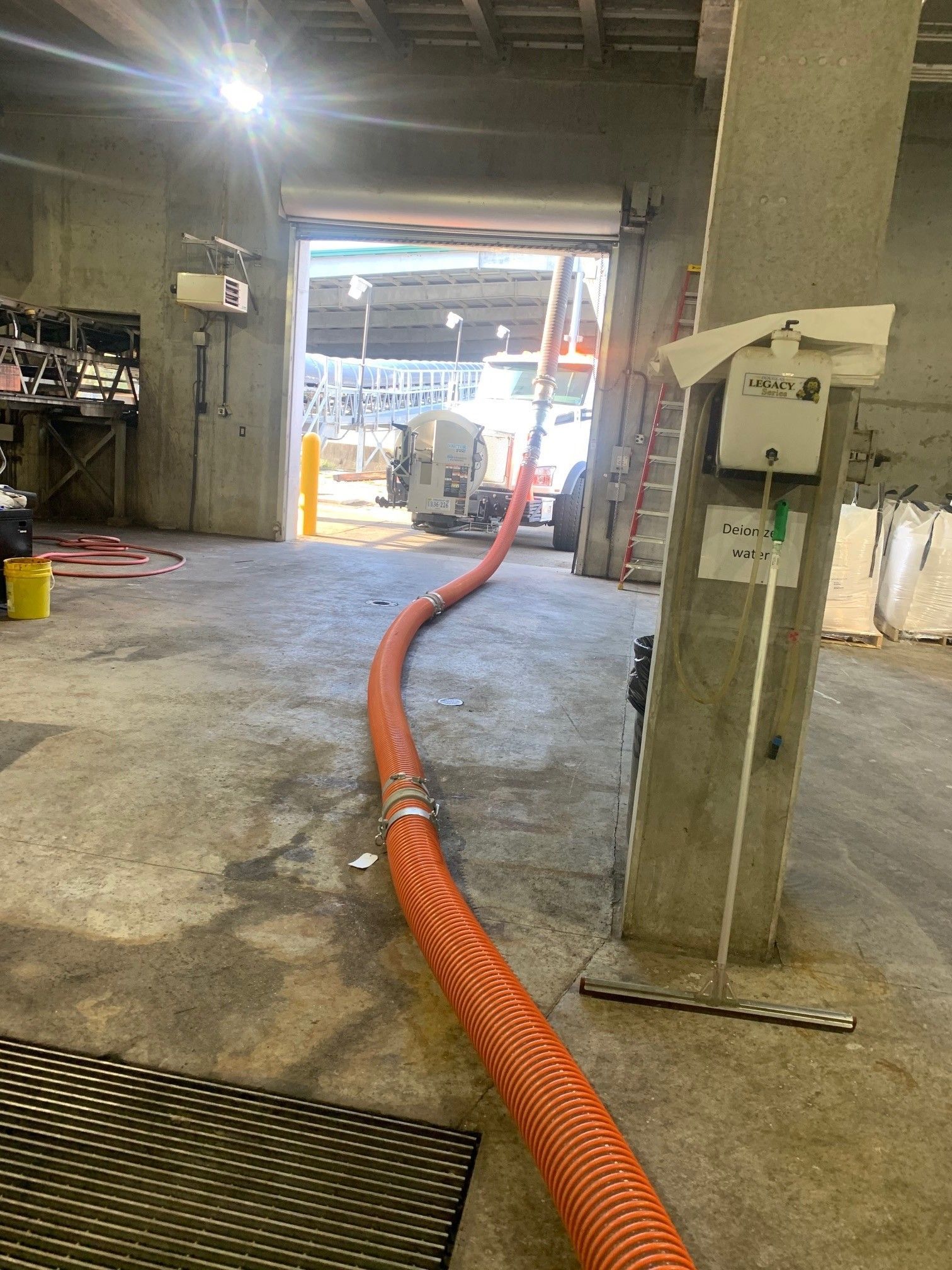 Orange hose in a concrete garage, leading to an open doorway with a work vehicle outside.