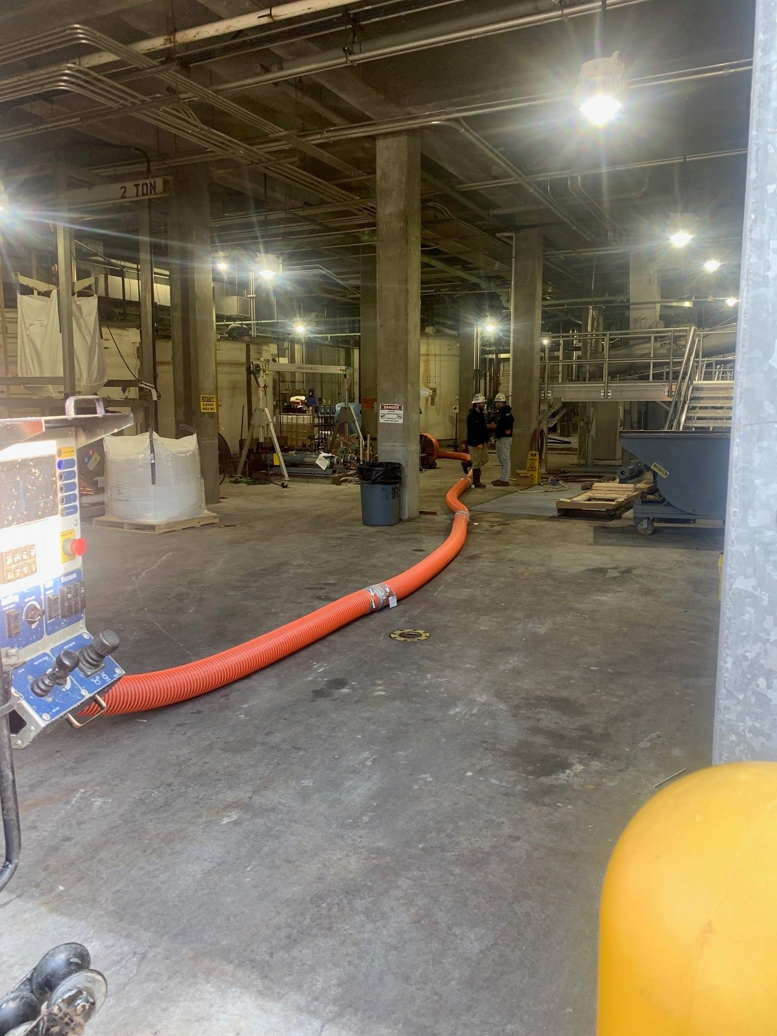 Industrial warehouse interior with orange hose across floor, equipment, and bright overhead lights