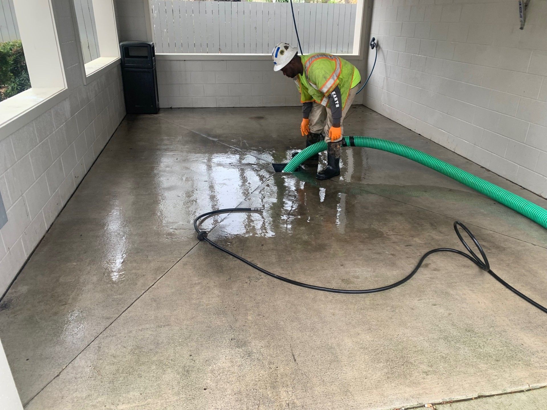 Worker pressure-washing a wet concrete floor in a covered patio area