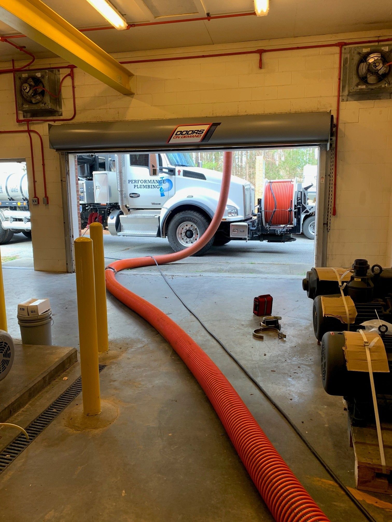 Orange hose running from a garage doorway to a vacuum truck outside