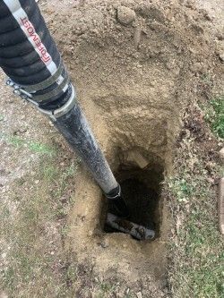 Black pole beside a freshly dug hole in dry dirt and grass