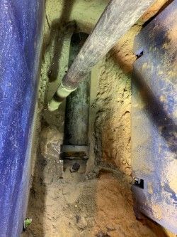 Narrow utility shaft with pipes and dusty walls, lit by a flashlight or work light