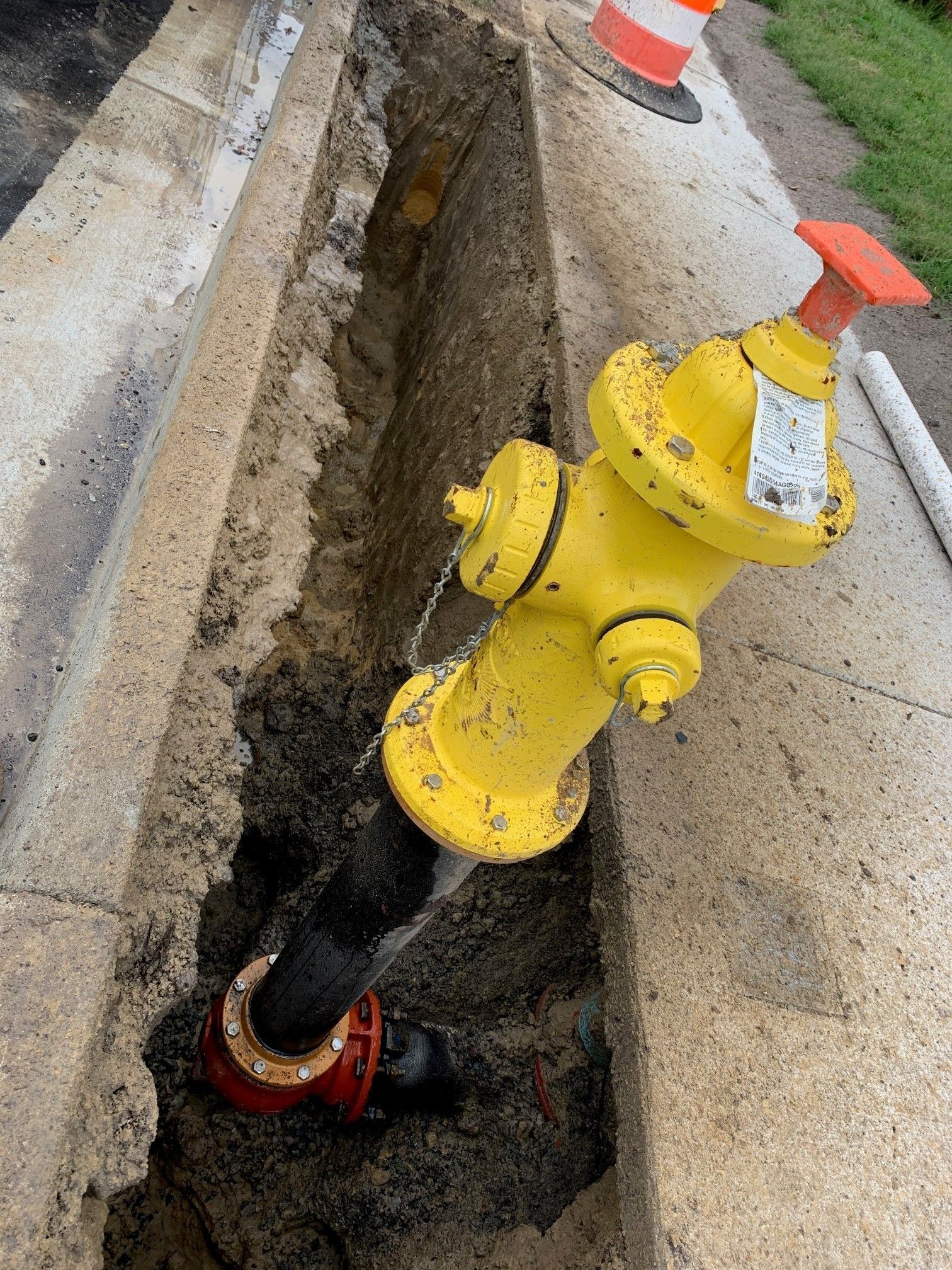 Yellow fire hydrant beside a trench in a sidewalk near orange traffic cones