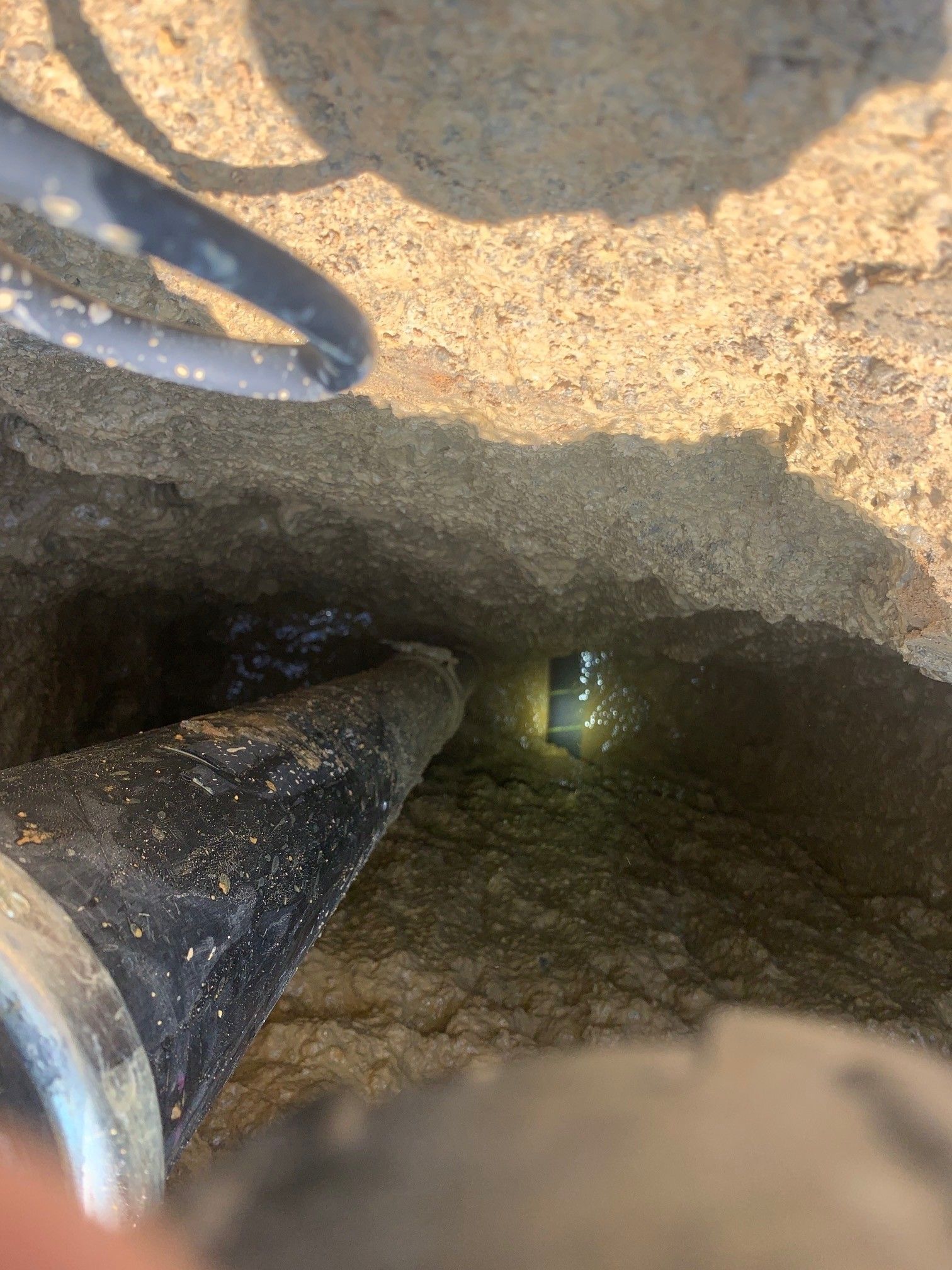 Metal pipe inside a rough dirt hole with dark opening and a small light at the far end