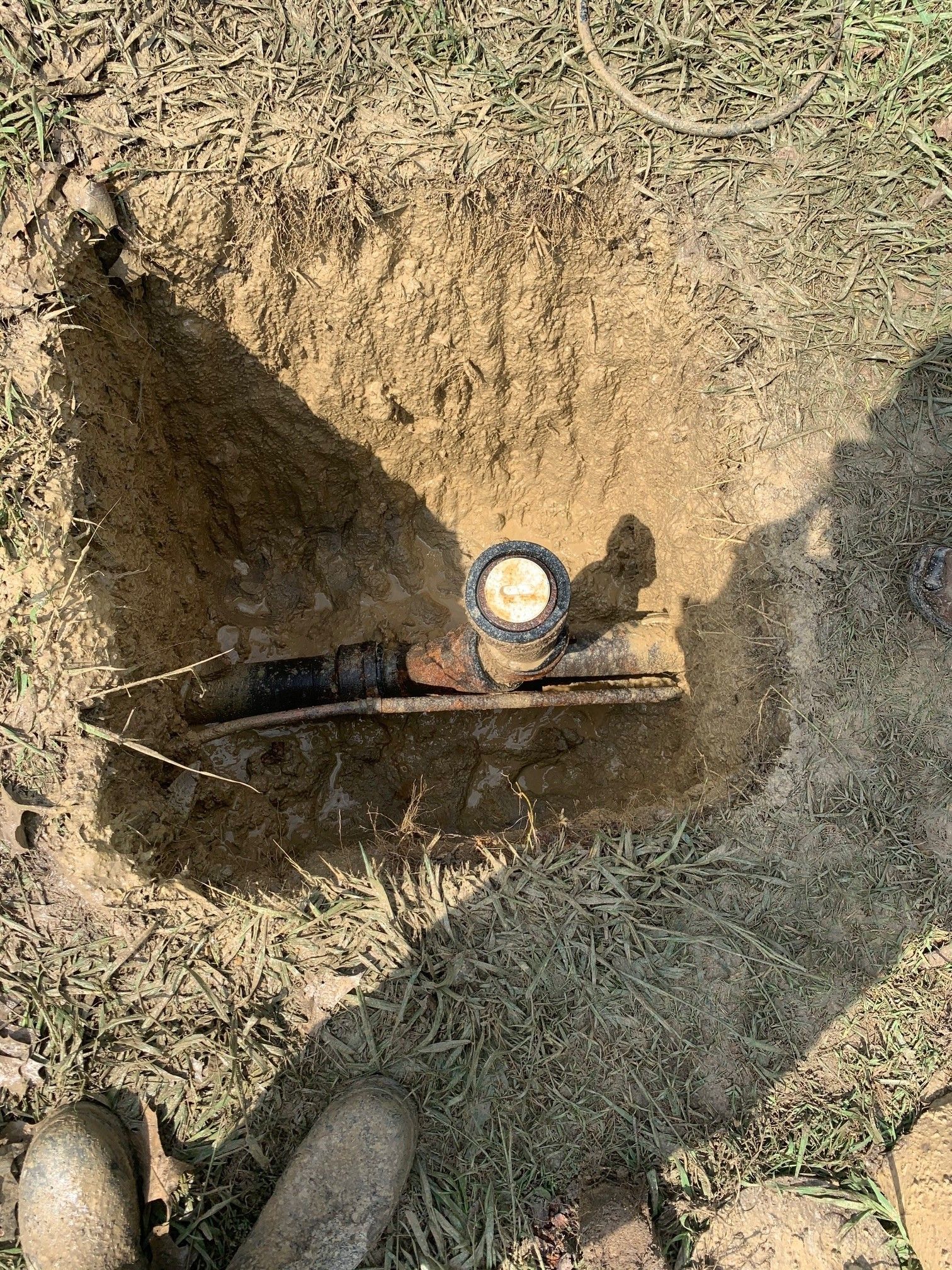 Shovel in a dirt hole with a round gauge and black tool, viewed from above outdoors.