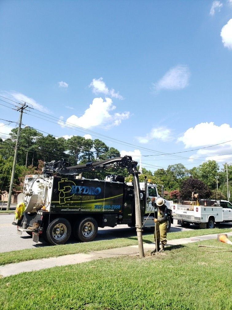 Utility trucks and workers on a roadside under a bright blue sky, with trees and power lines nearby.