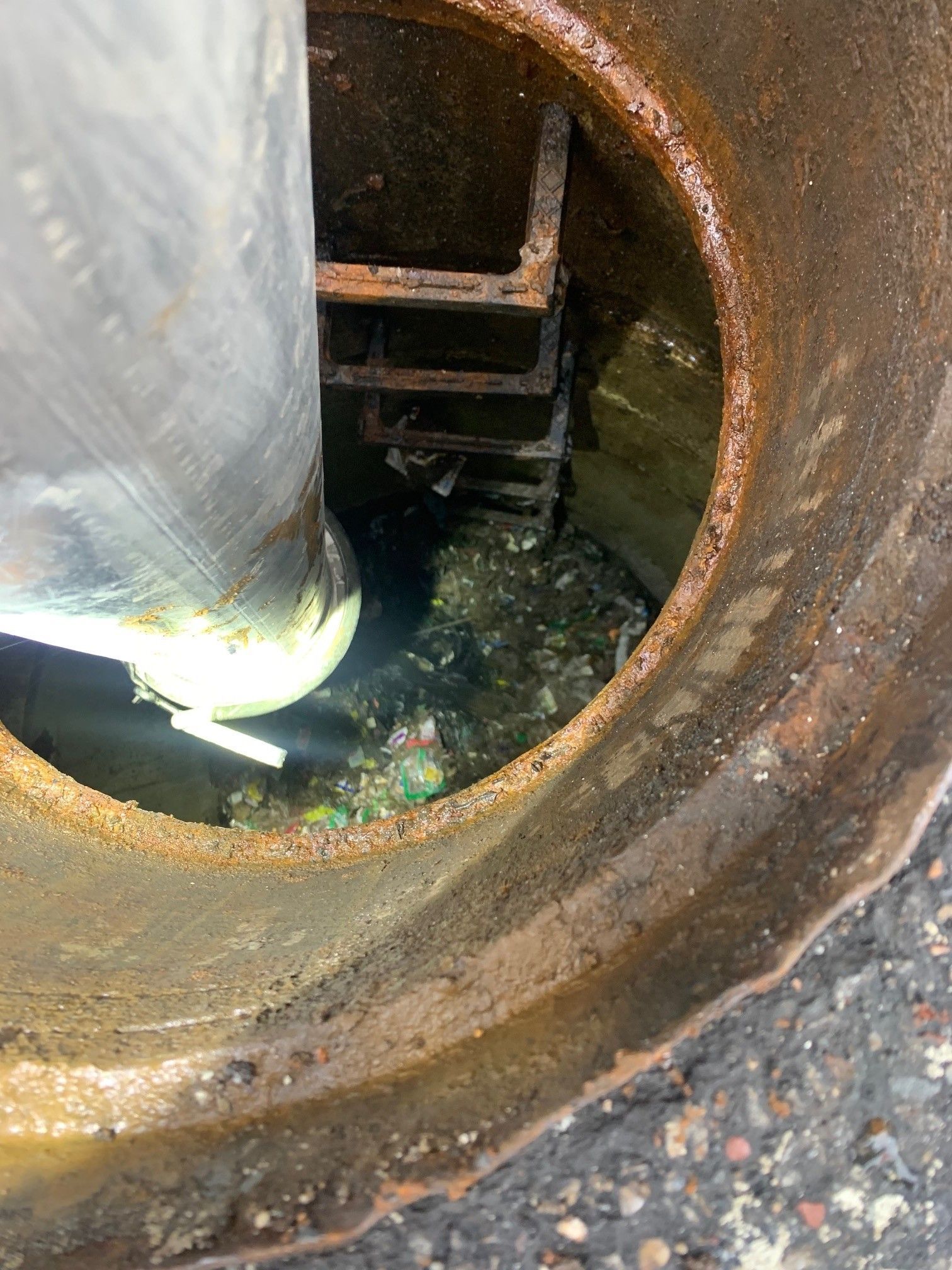 Rusty manhole opening with a pipe inside and standing water below