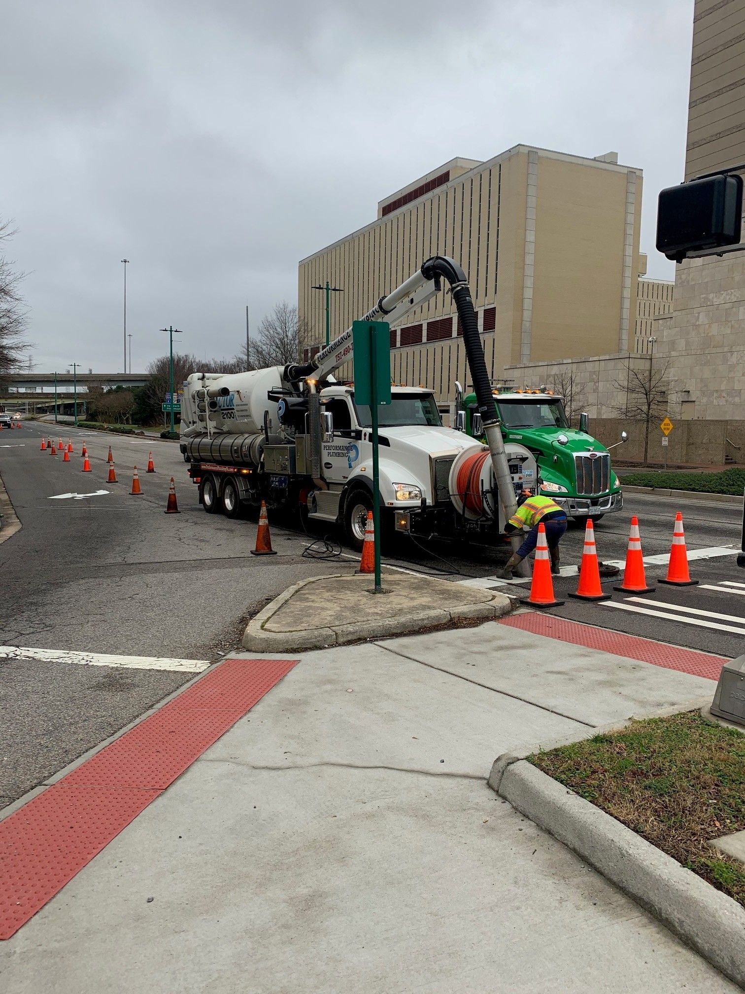 Construction truck and concrete pump blocking a street corner with orange cones on a cloudy day