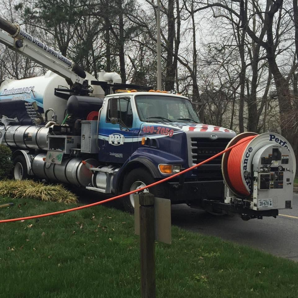 Blue utility truck with hose reel parked on grass near trees, with orange hose in front