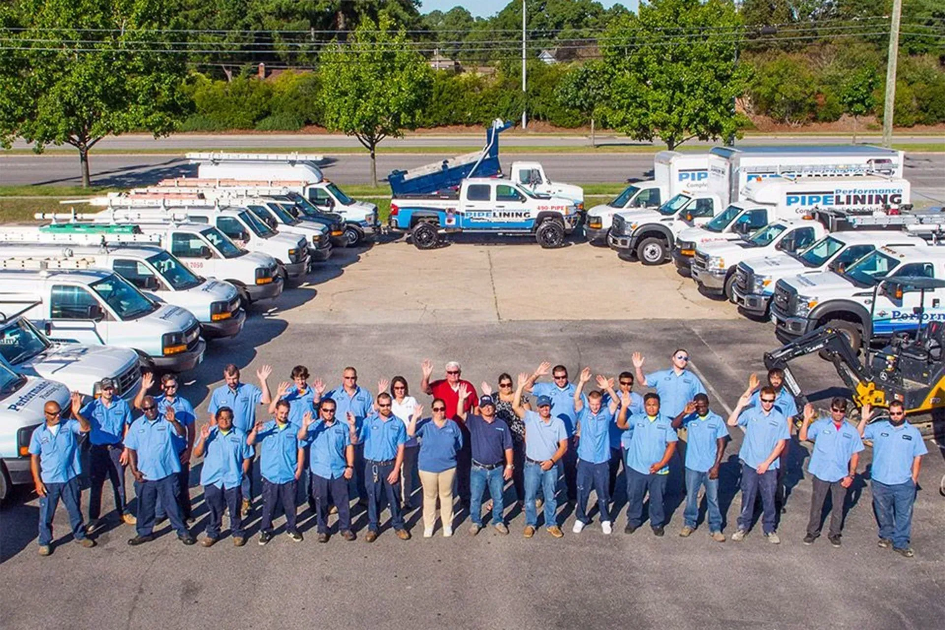 Fleet of white utility trucks with a group of workers in blue uniforms posing in front