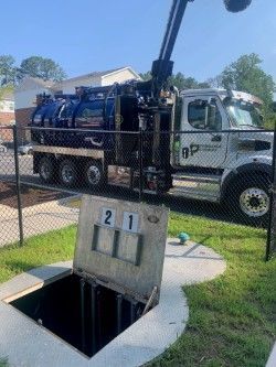 Vacuum truck parked beside an open utility vault near a chain-link fence on a sunny day