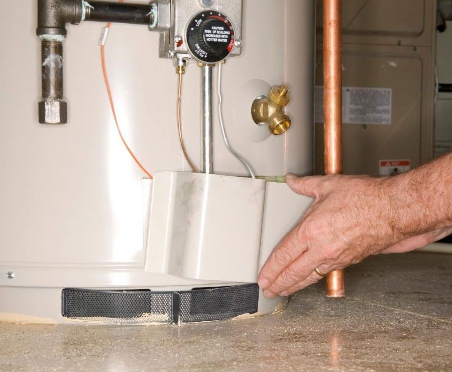Plumber’s hand holding a copper pipe near a water heater and drain pan in a utility room