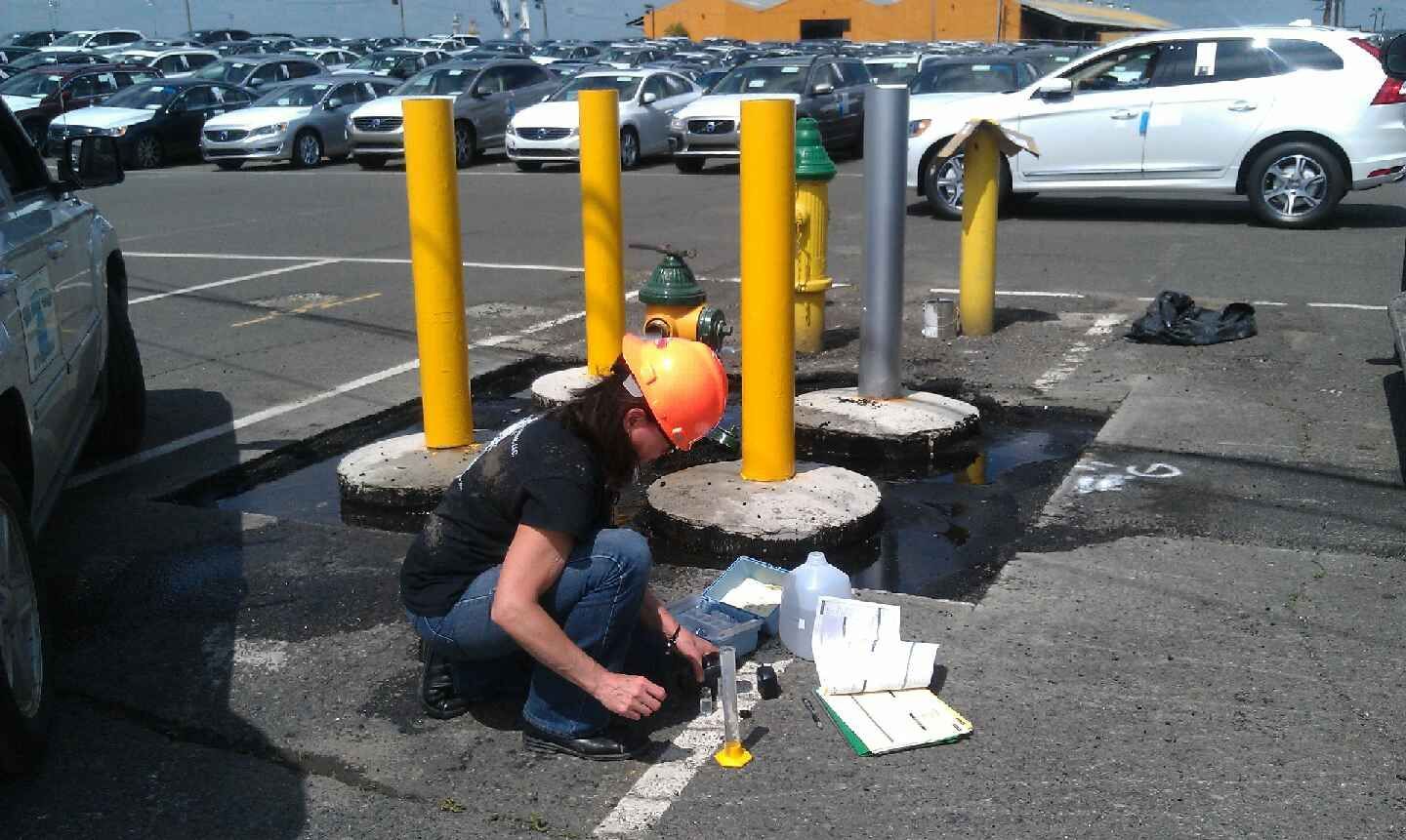 A man wearing a hard hat is kneeling down in a parking lot