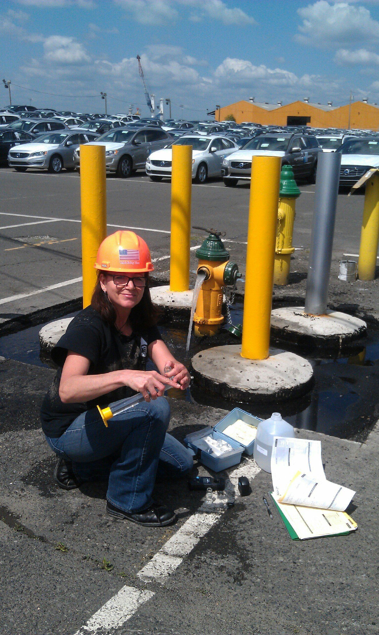 A woman wearing a hard hat is kneeling down in a parking lot