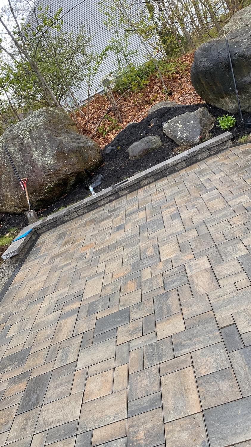 Stone patio next to a hillside with rocks, black mulch, and a chain-link fence.