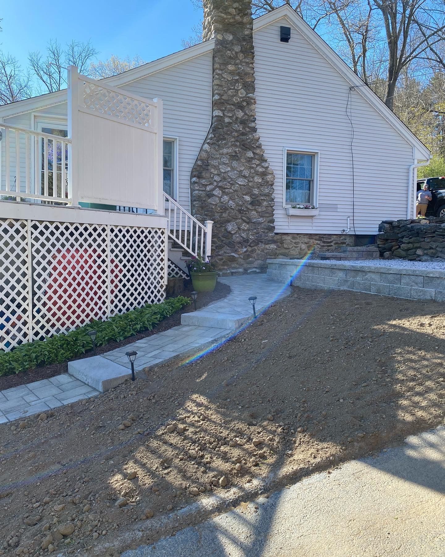 White house with stone chimney, walkway, and decorative white lattice deck.