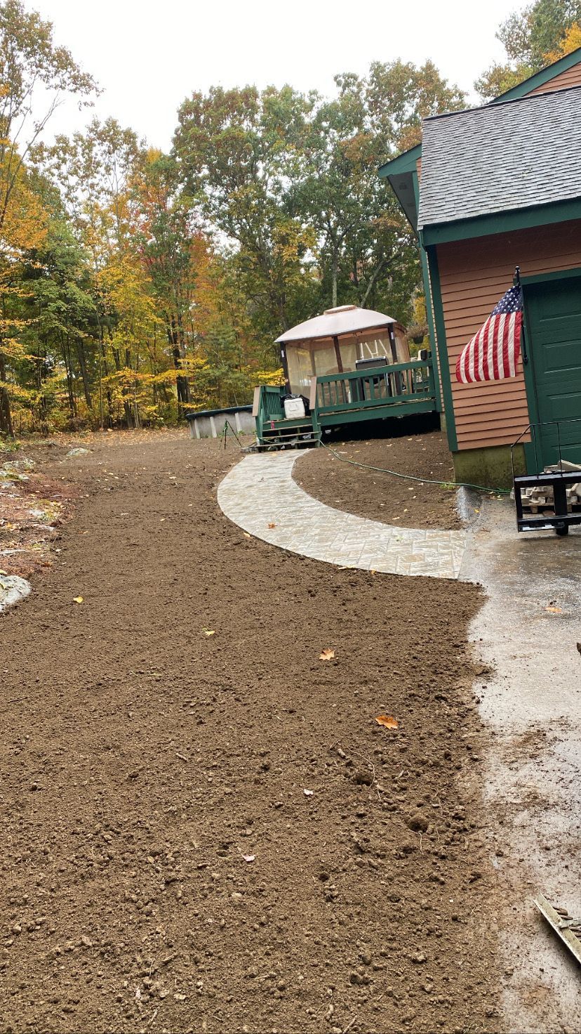 A gravel path curves toward a deck and a building with a waving American flag. Autumn trees surround.