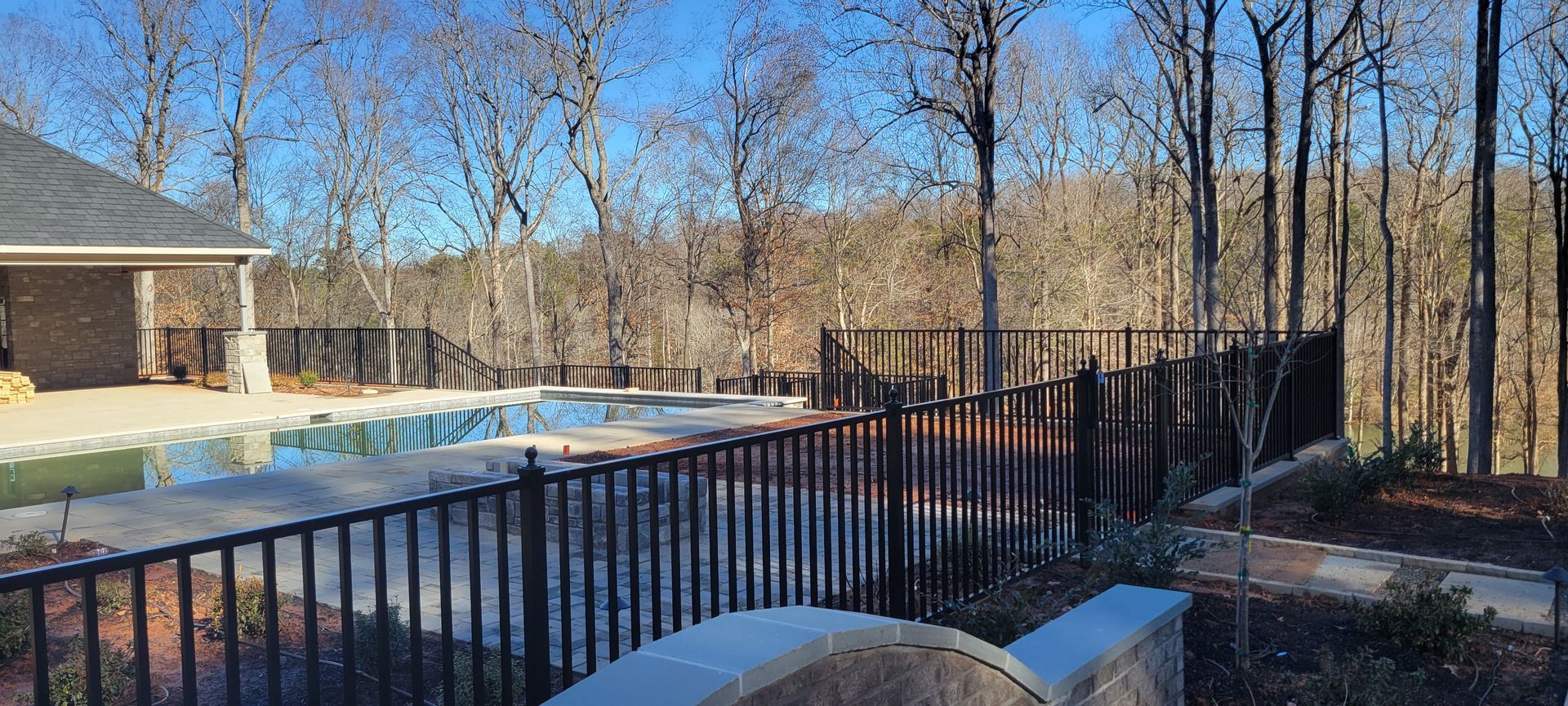 A fence surrounds a swimming pool in the middle of a forest.