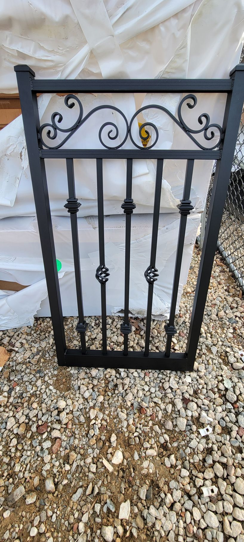 A black wrought iron gate is sitting on top of a pile of gravel.