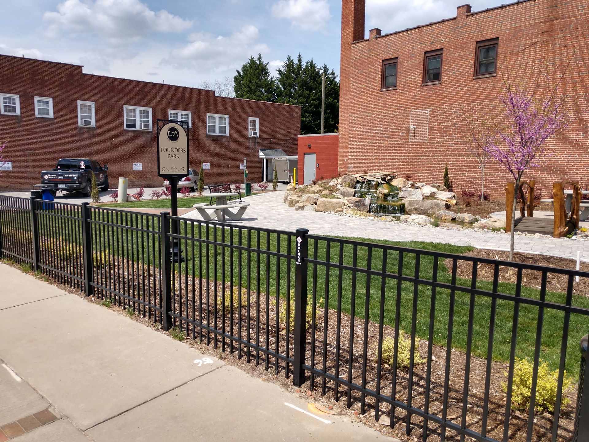 A fence surrounds a park with a brick building in the background.