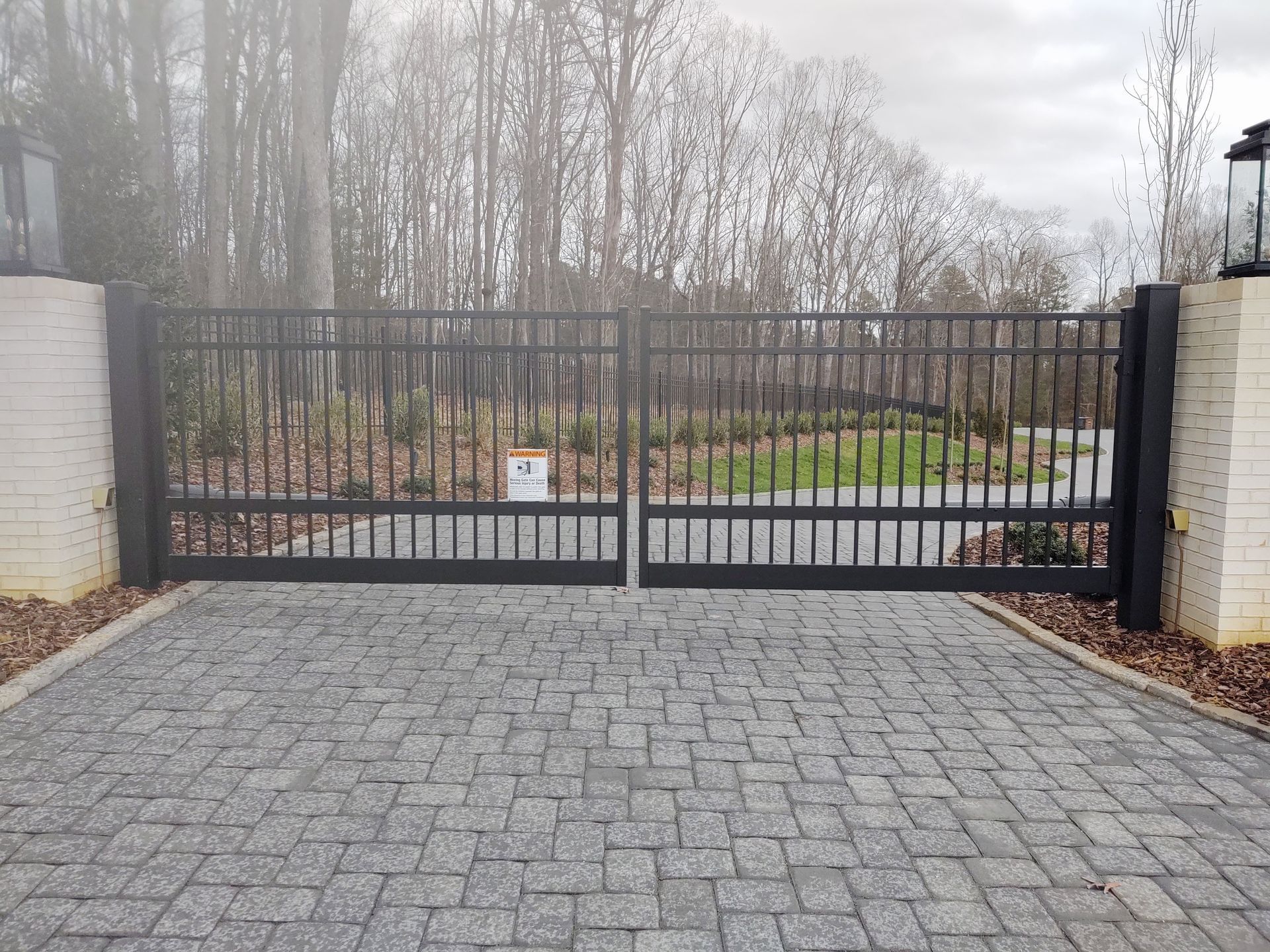 A black gate is open to a driveway with trees in the background.