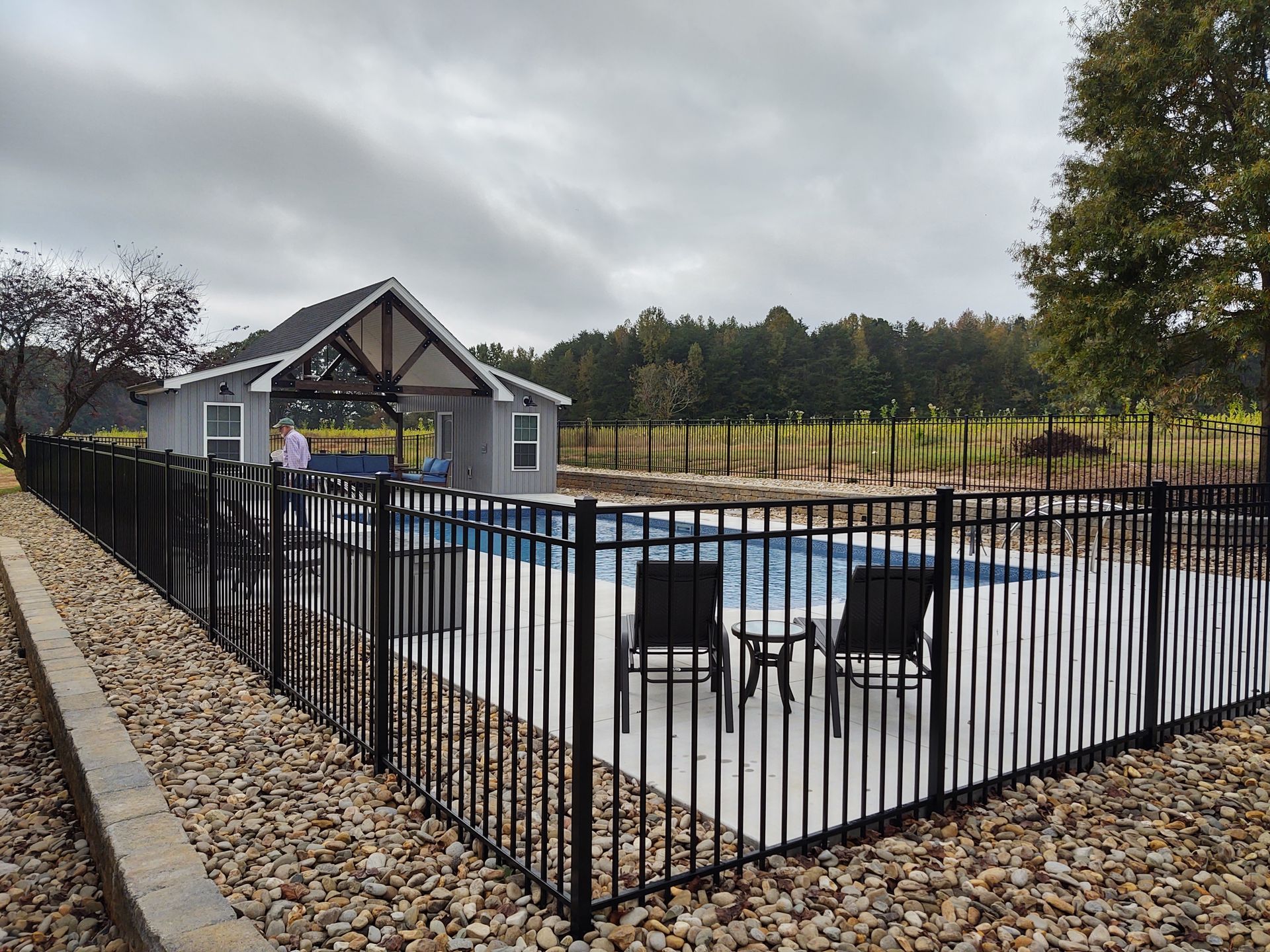 A fence surrounds a swimming pool with a gazebo in the background