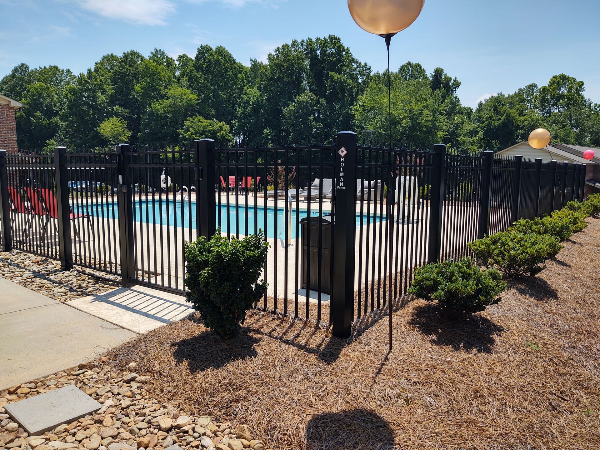 A black fence surrounds a swimming pool with trees in the background