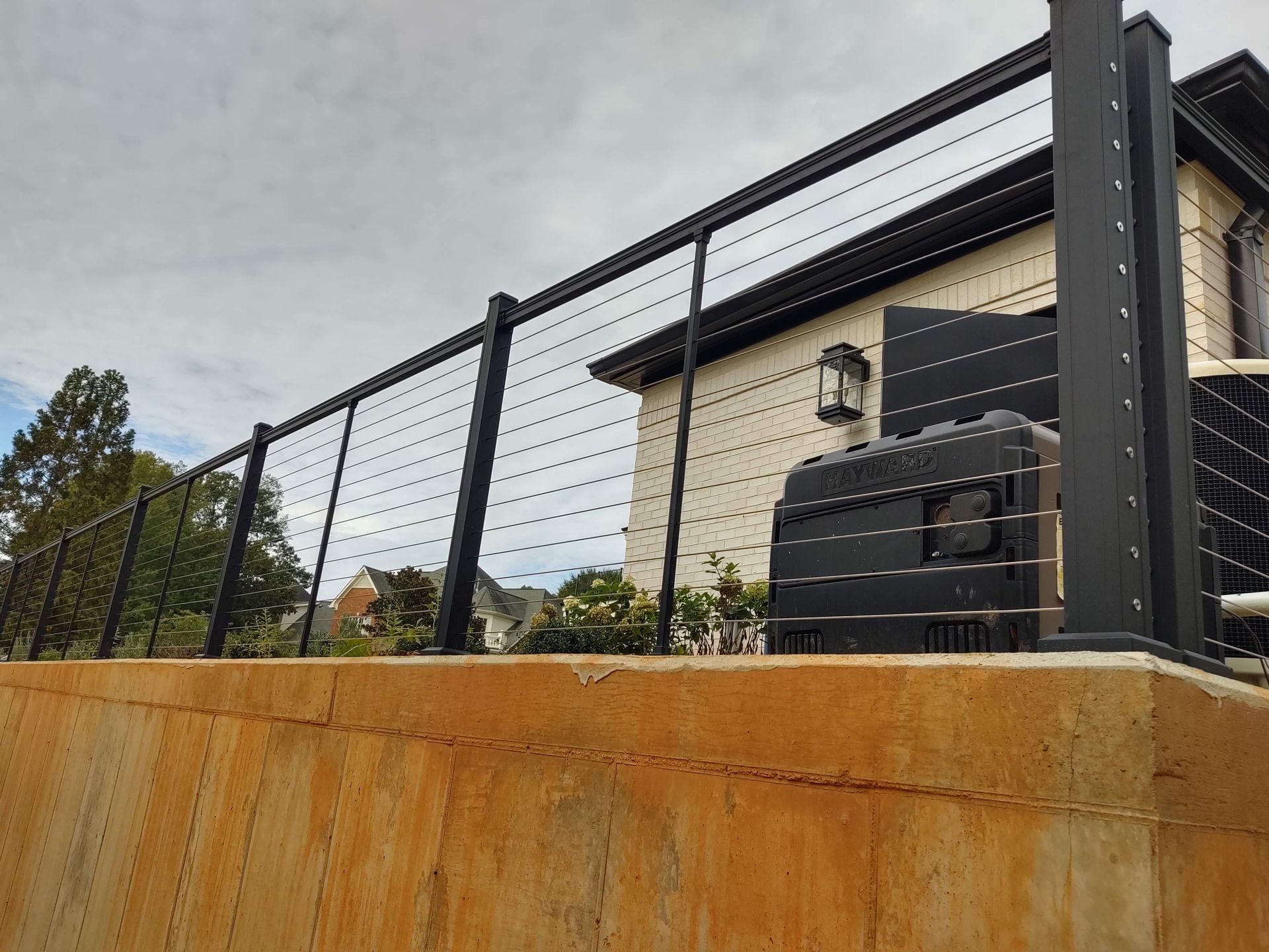 A black wire fence surrounds a concrete wall in front of a house.