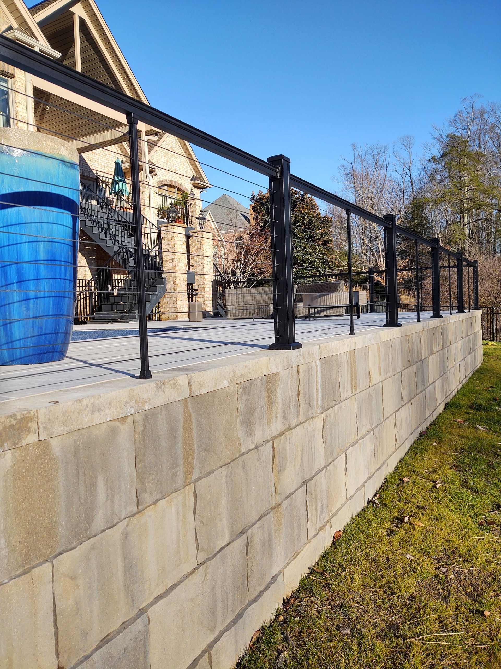 A brick wall with a black railing and a blue bucket in front of a house.