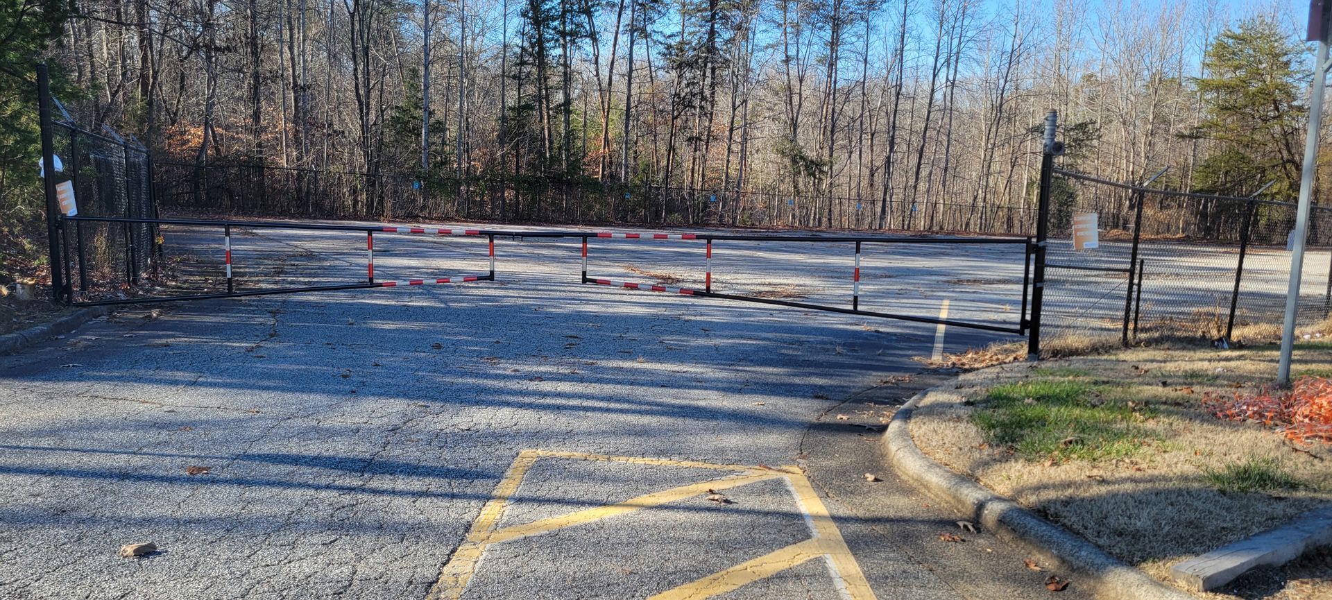 a parking lot with a fence and trees in the background