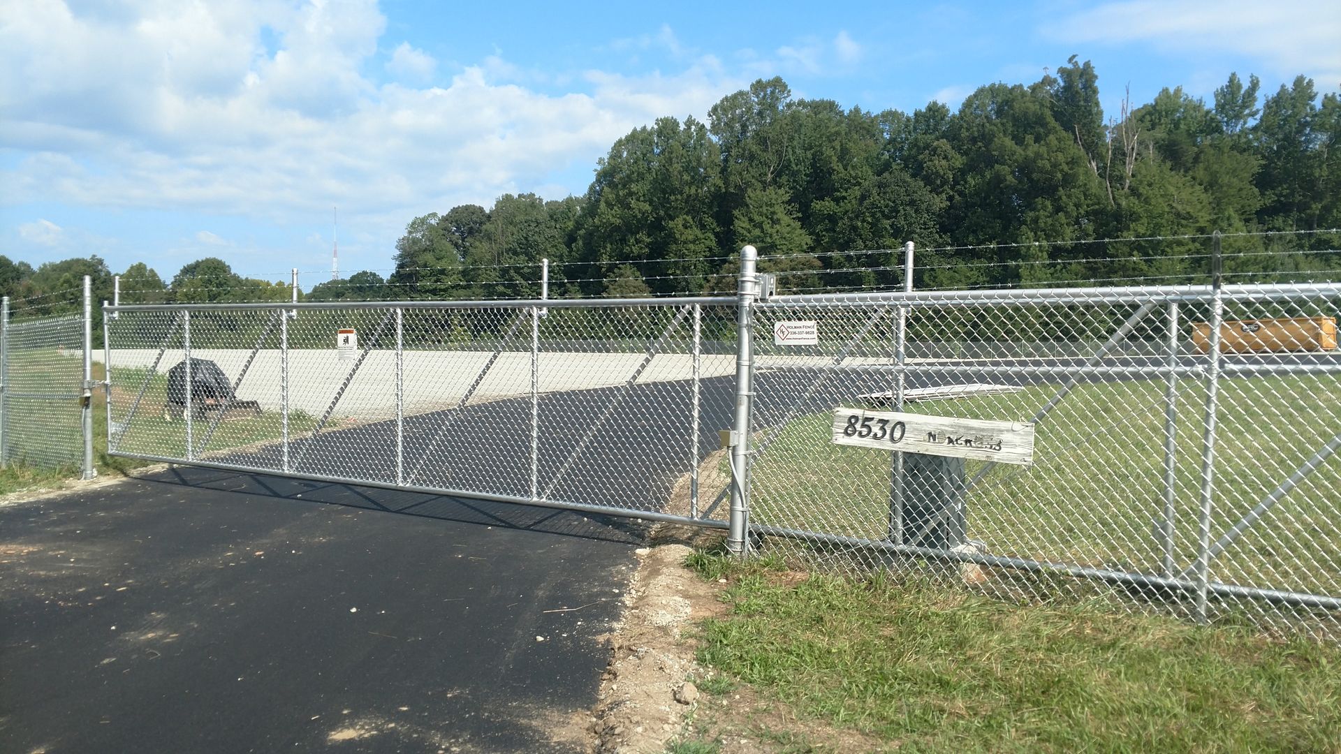 a chain link fence surrounds a dirt road with trees in the background