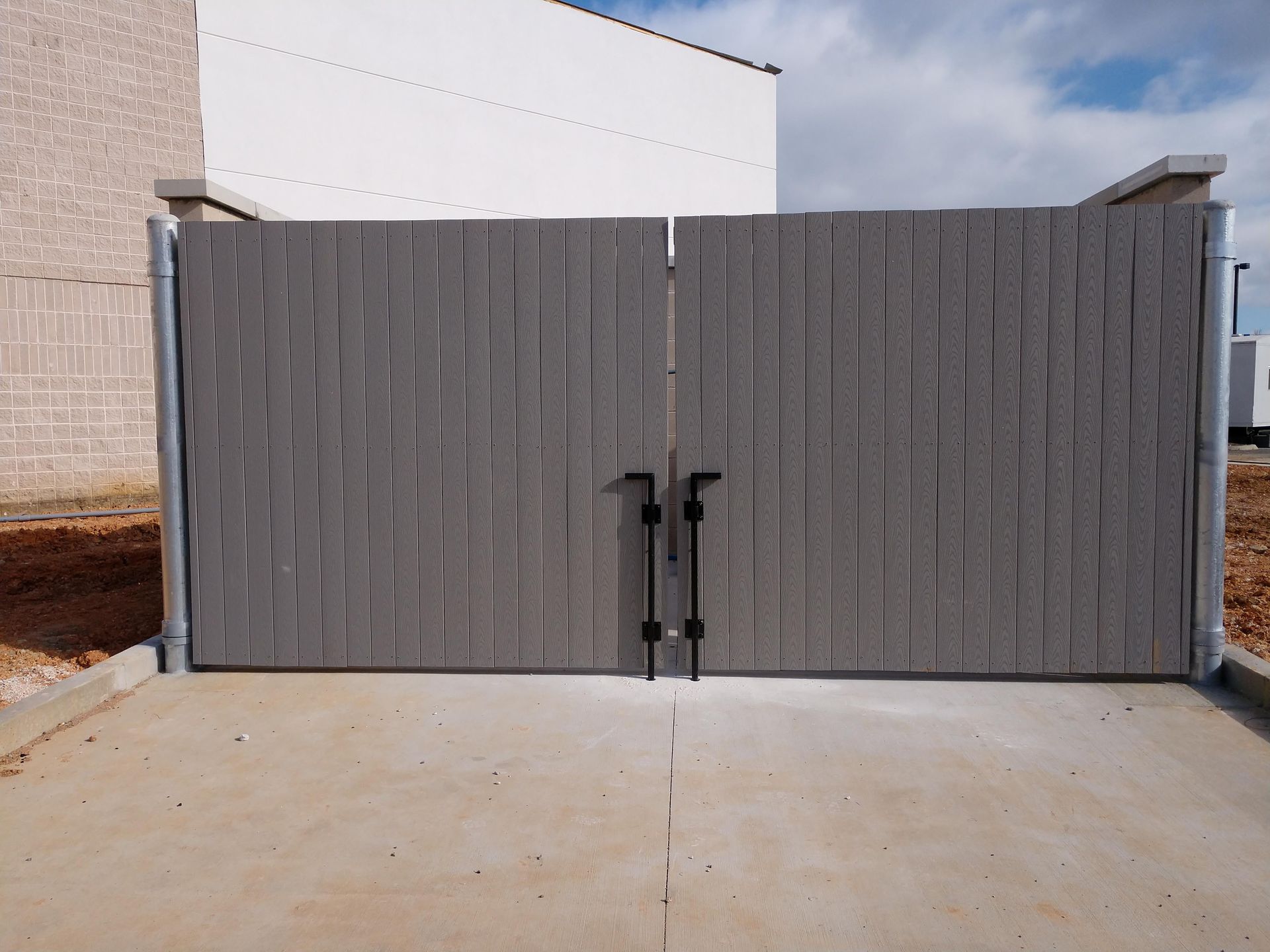 a gray wooden gate open to a concrete driveway
