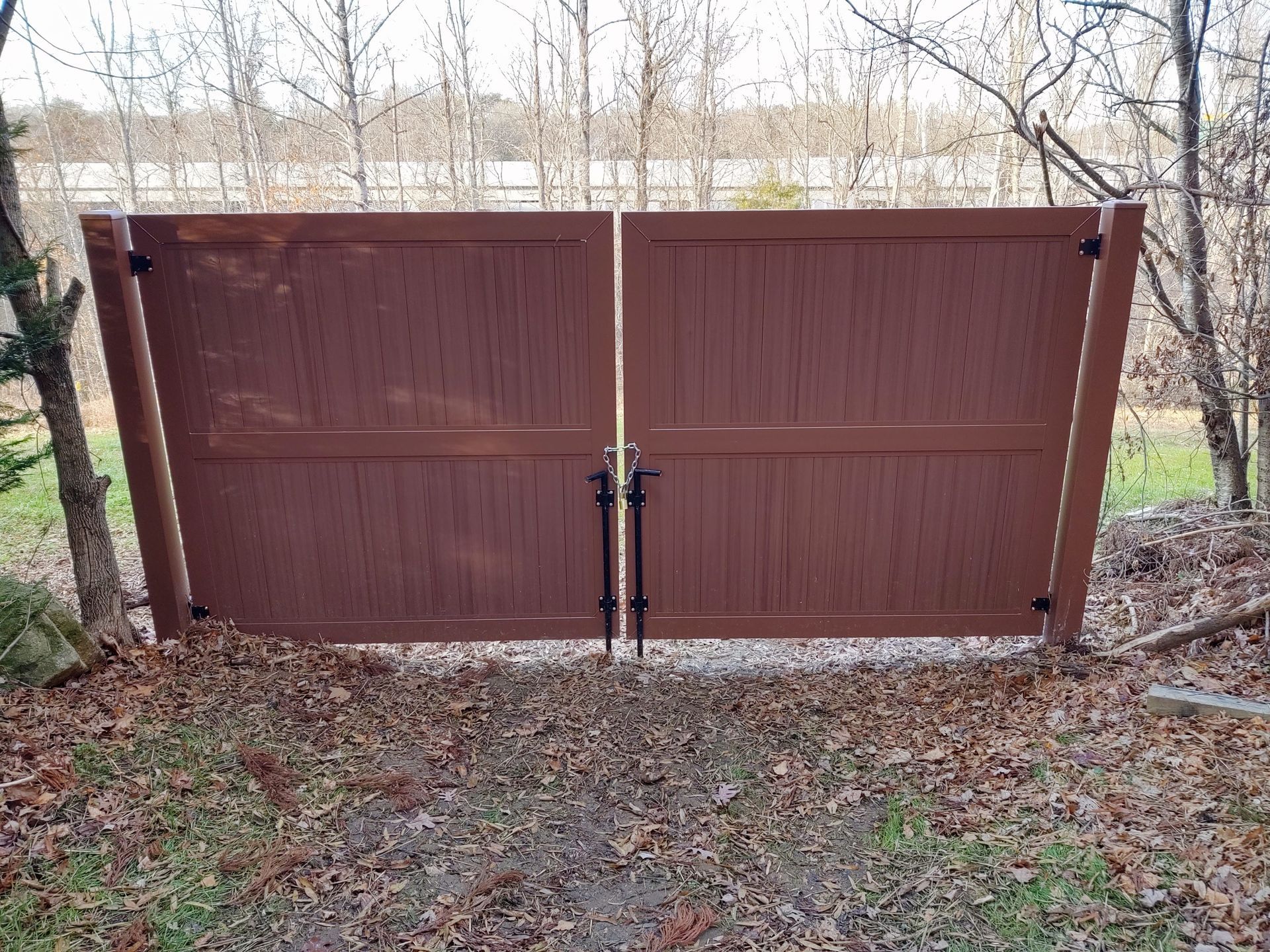 a brown wooden gate sitting on top of a dirt road next to trees