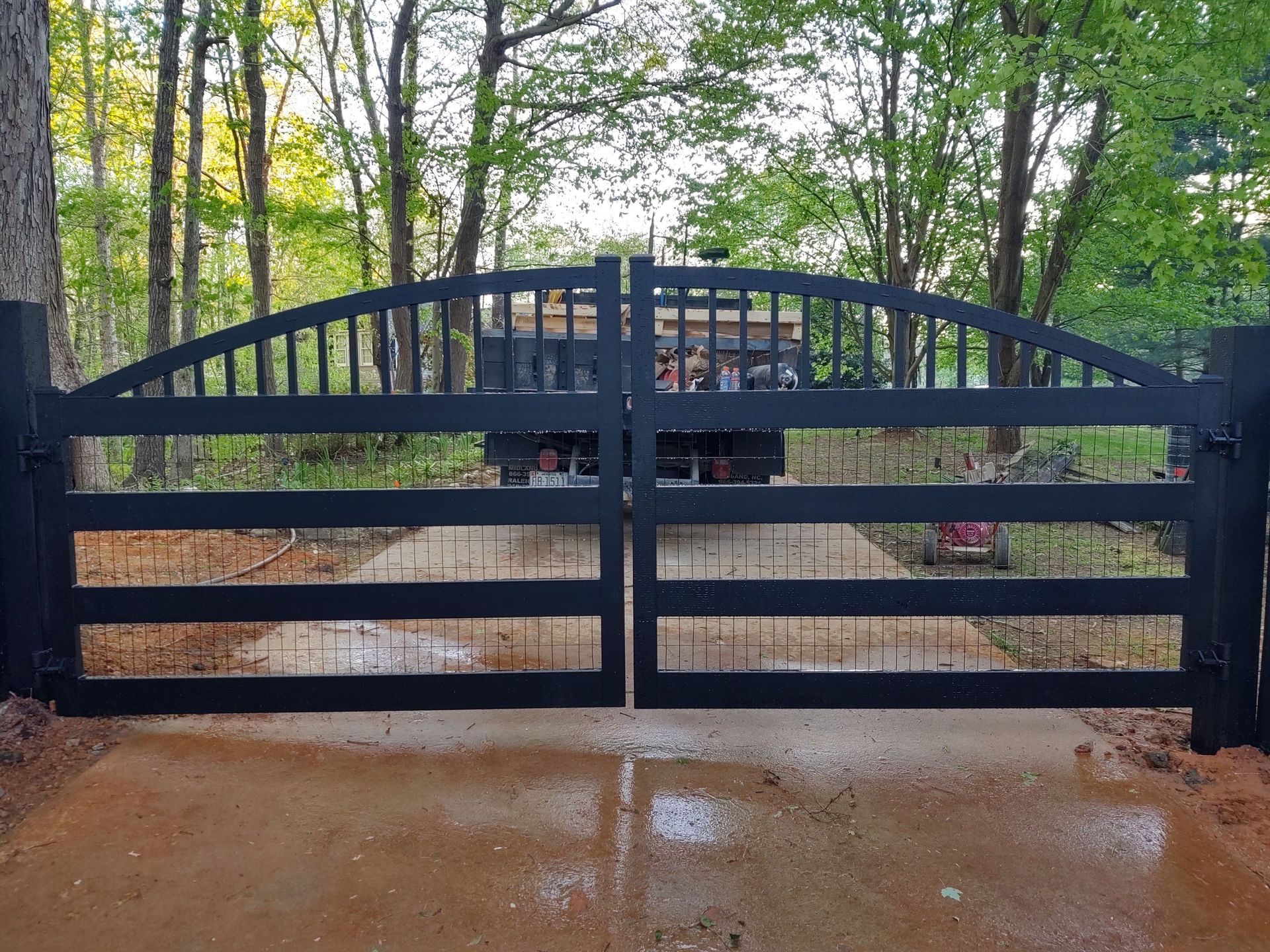 a black gate open to a driveway with trees in the background