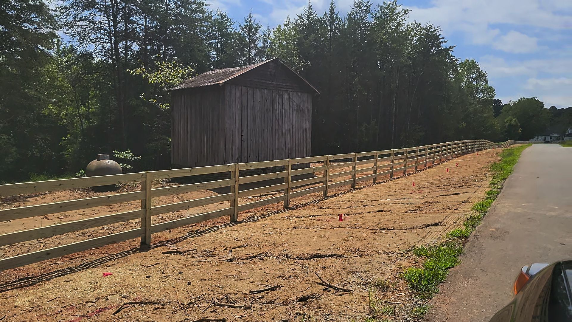 A wooden fence along a road with a shed in the background