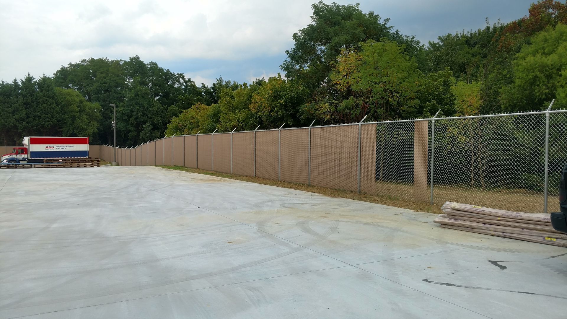 a chain link fence surrounds a parking lot with trees in the background