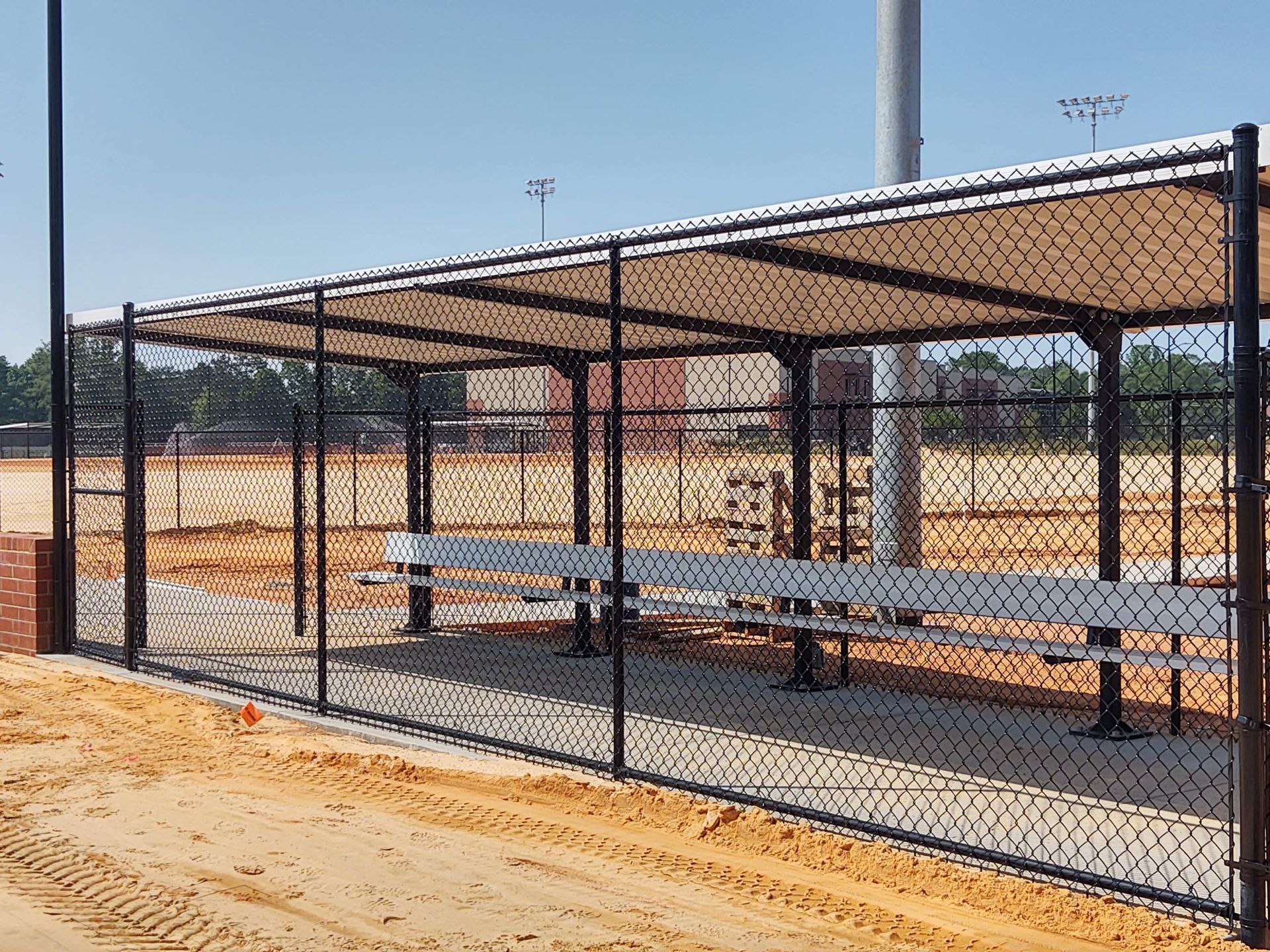a chain link fence surrounds a shelter with benches on a baseball field