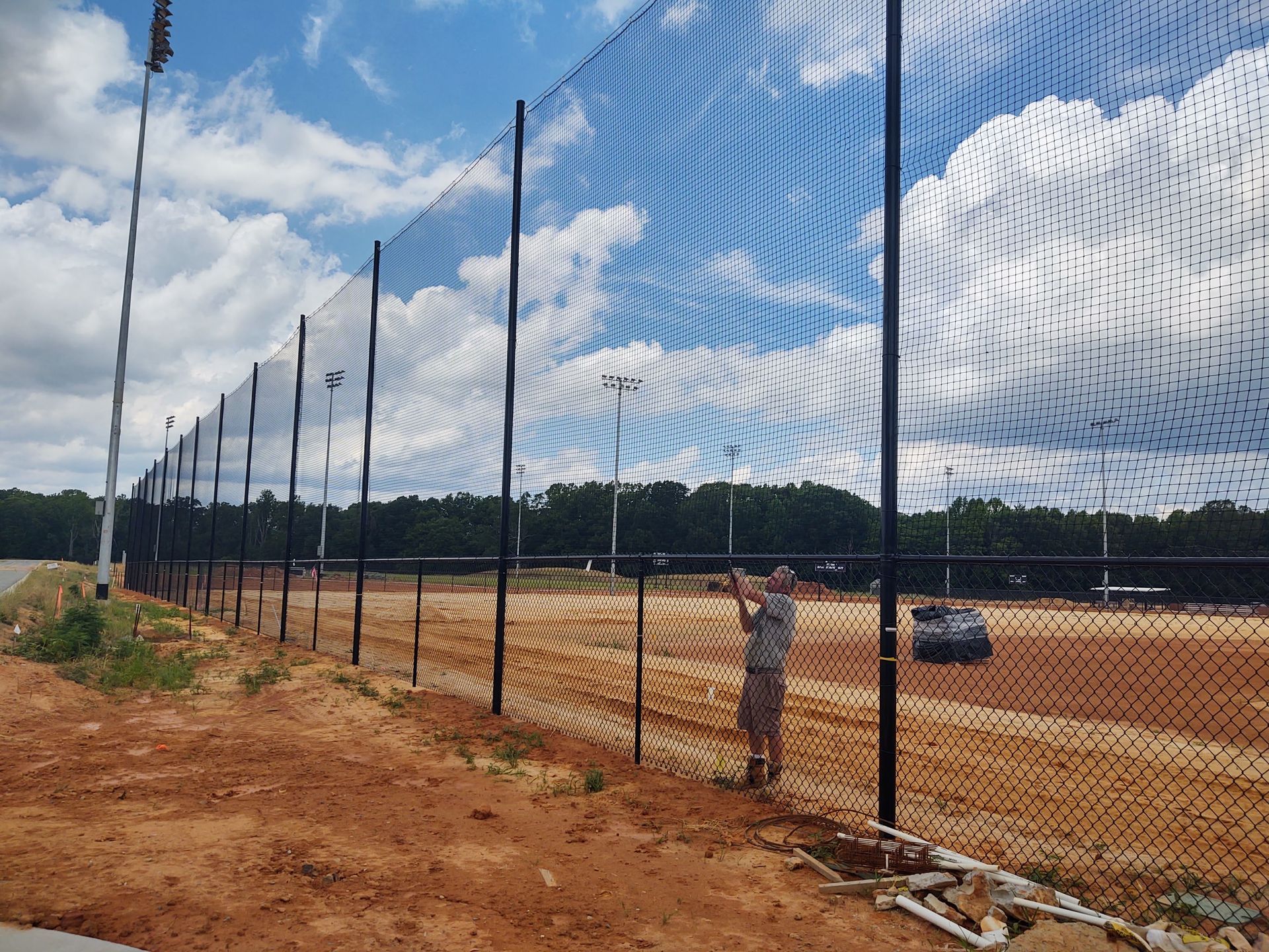 a man standing behind a chain link fence looking at a baseball field