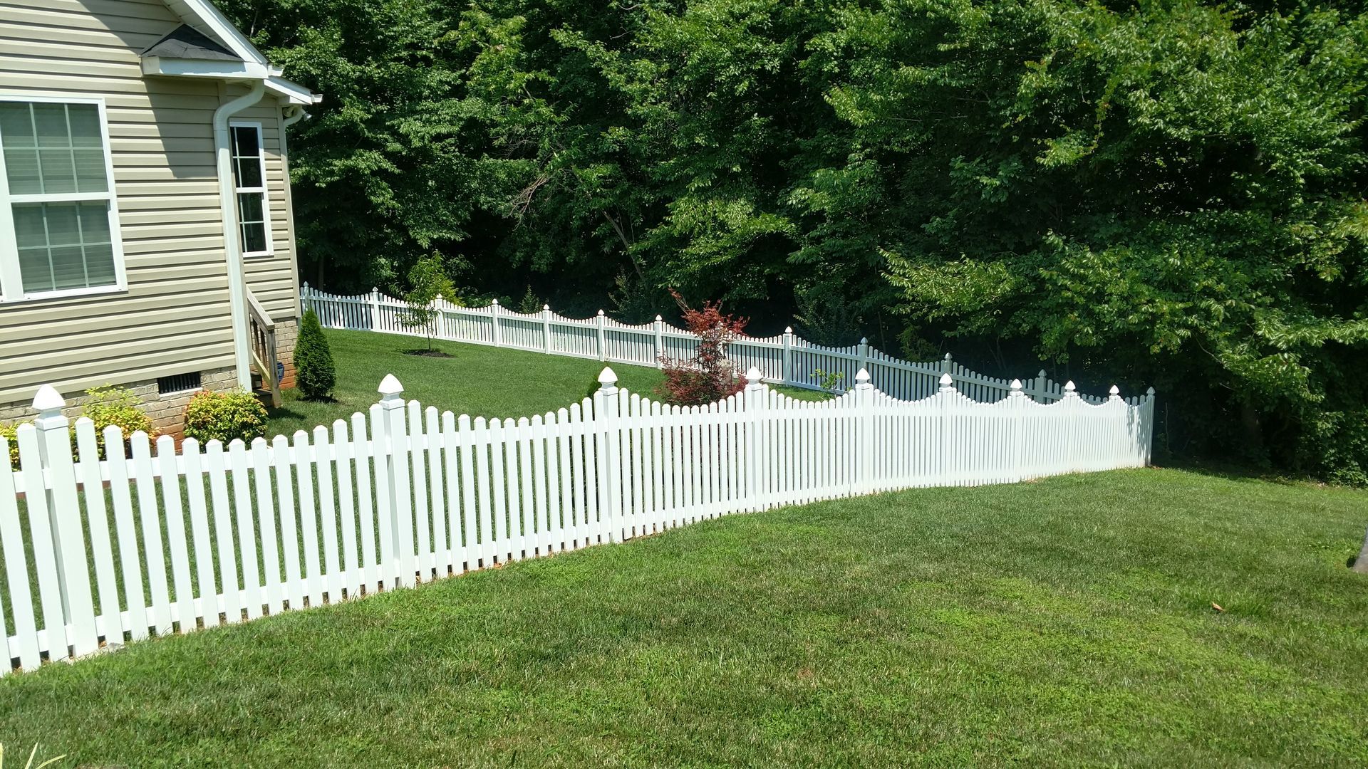a white picket fence surrounds a lush green yard in front of a house