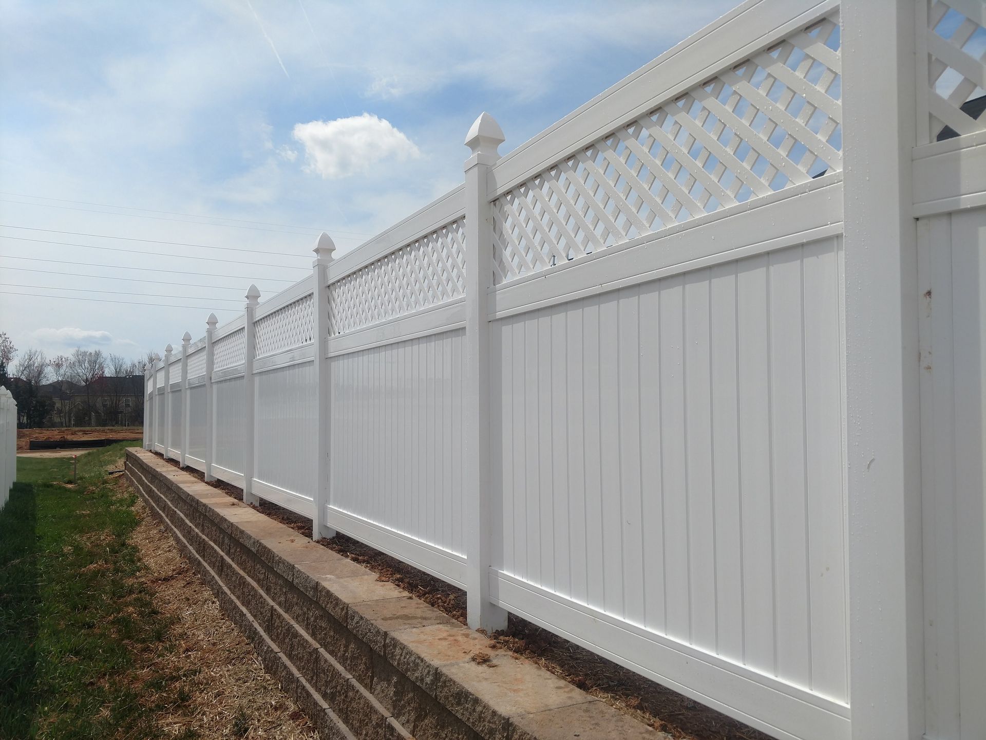 a white vinyl fence with a lattice design is sitting on top of a concrete wall