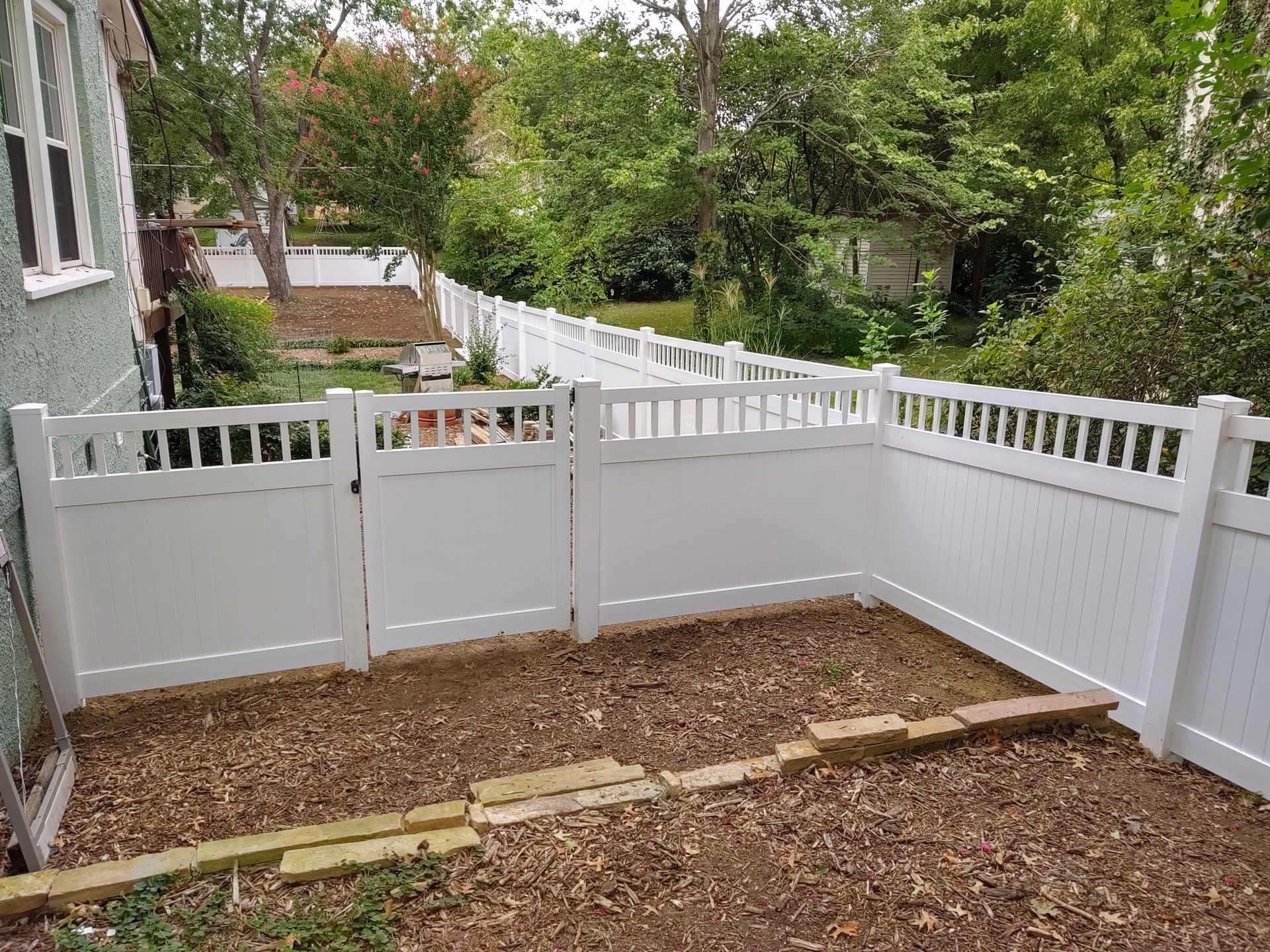 a white fence surrounds a backyard with a wooden walkway