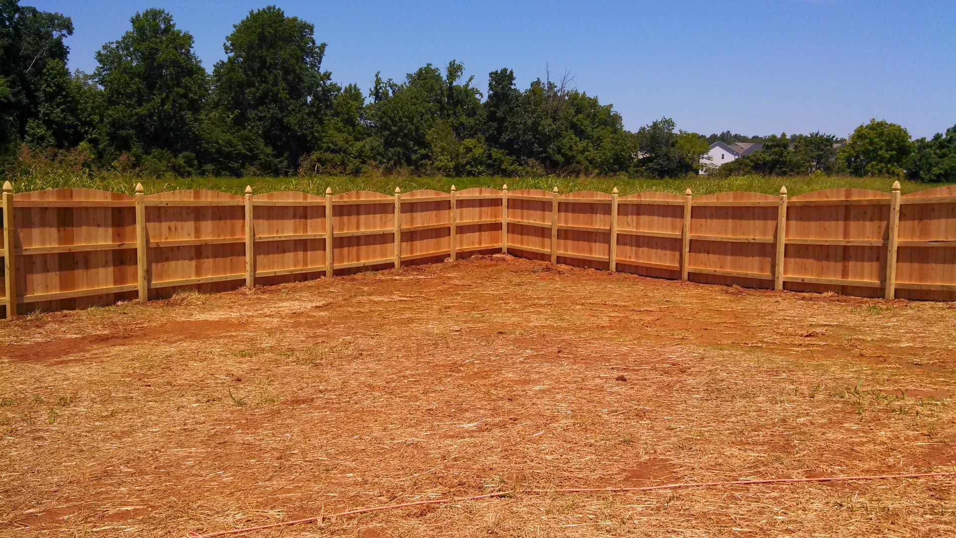 a wooden fence surrounds a dirt field with trees in the background