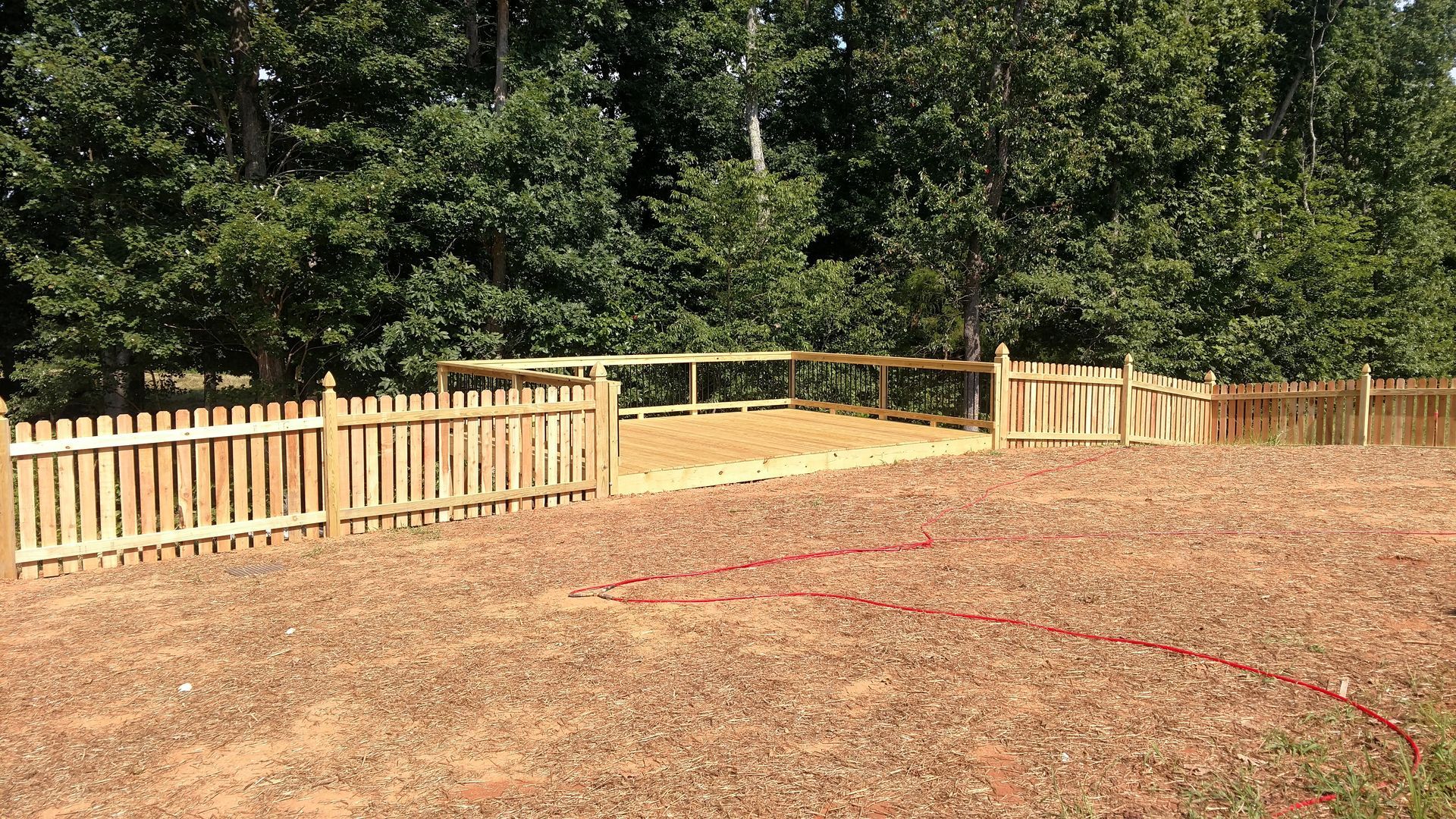 a wooden fence surrounds a dirt field with trees in the background