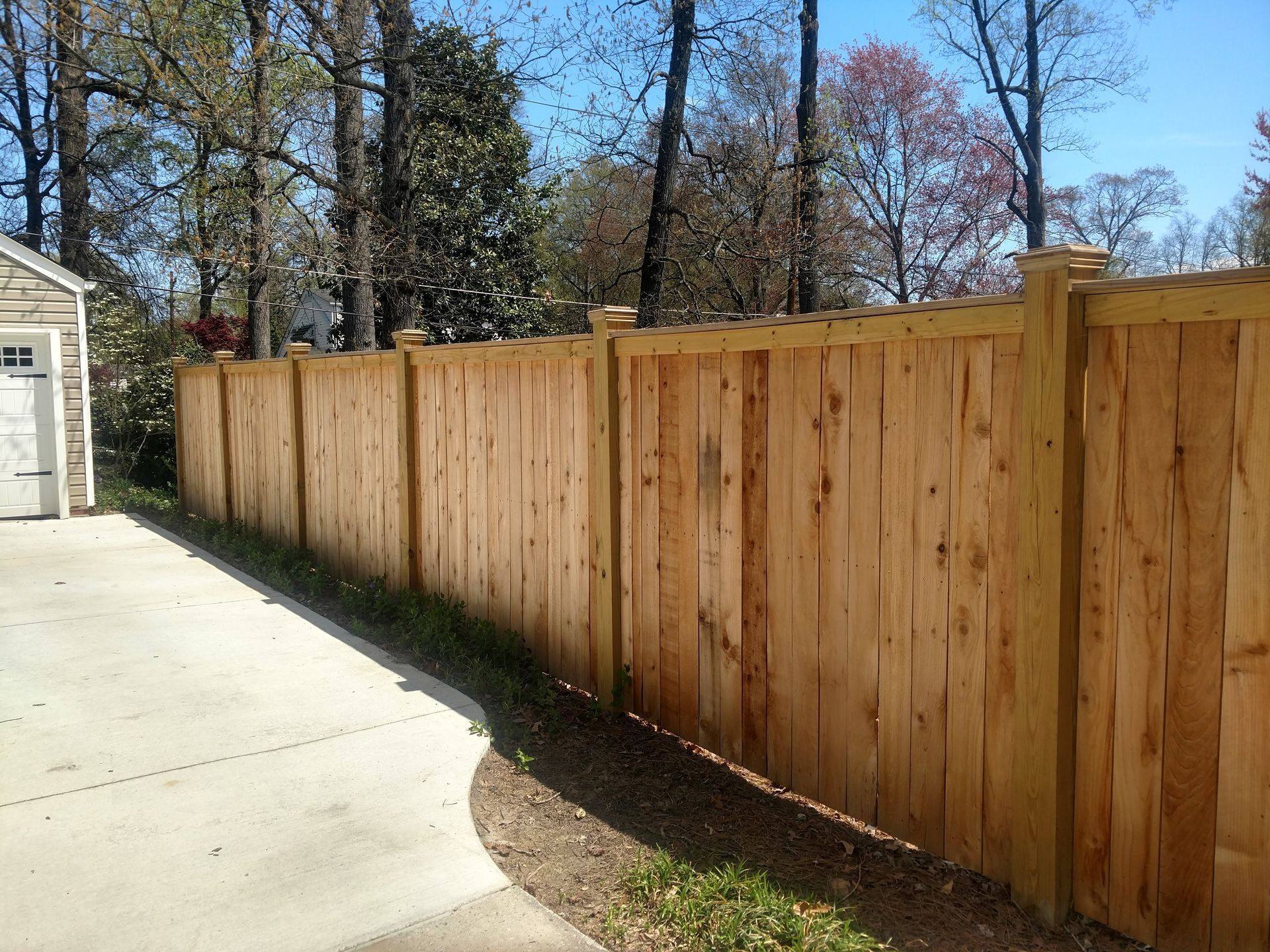 a wooden fence surrounds a driveway with trees in the background