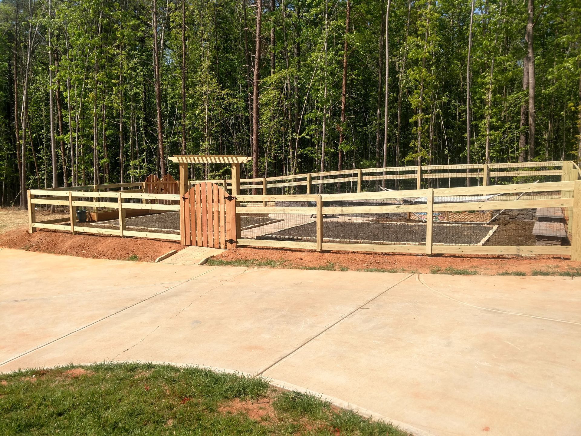 a wooden fence surrounds a concrete driveway with trees in the background