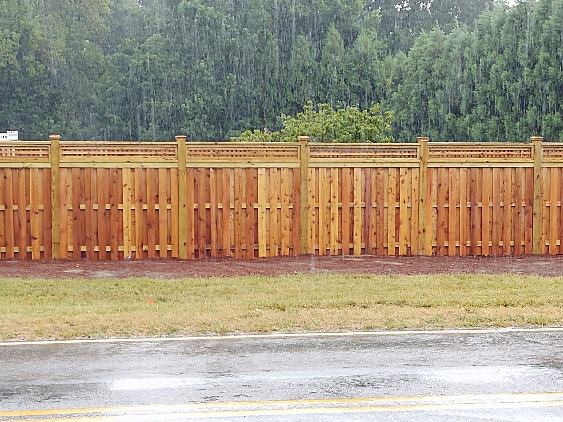 a wooden fence in the rain with trees in the background