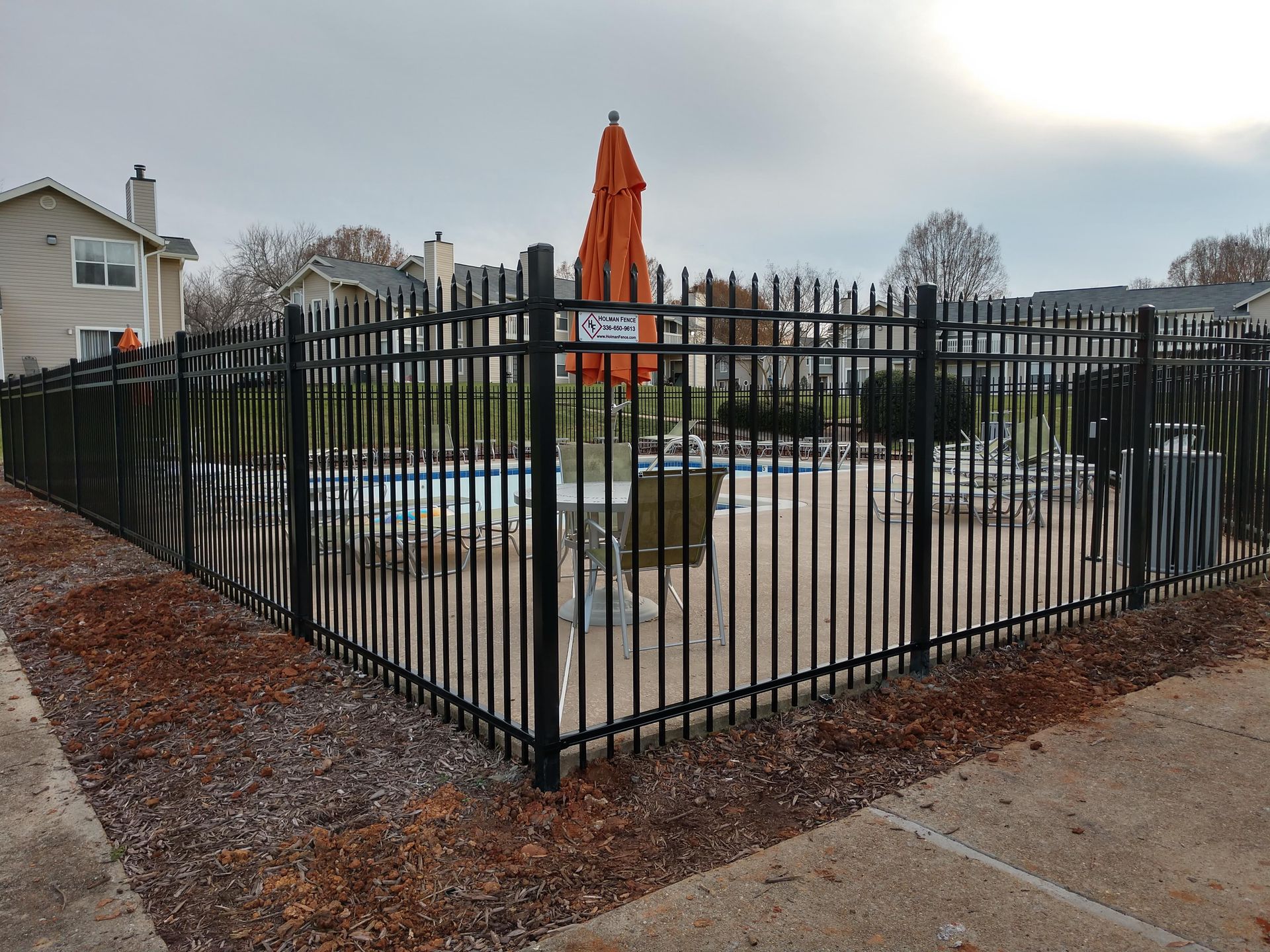 A black fence surrounds a swimming pool with an orange umbrella