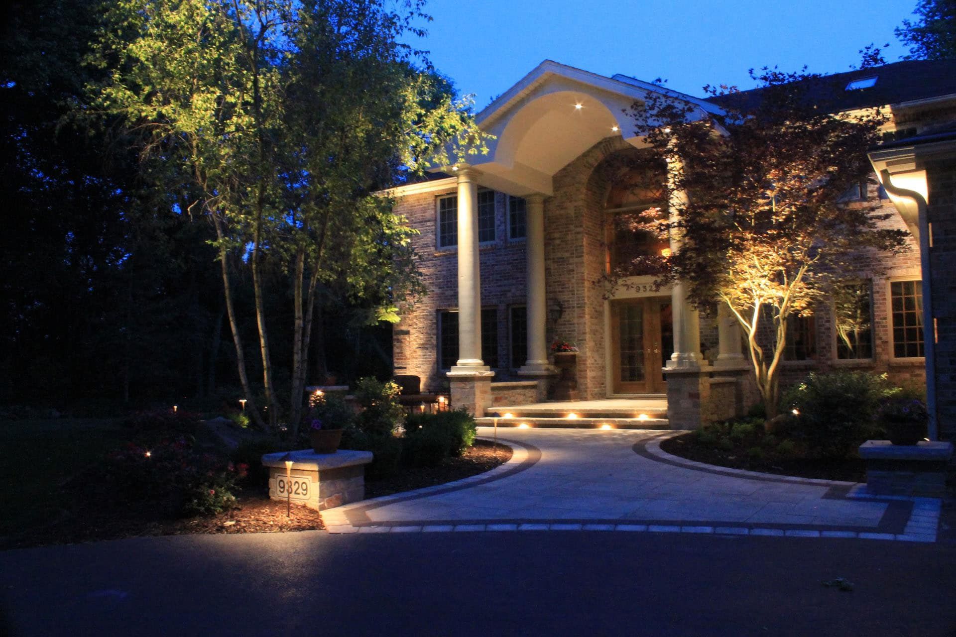 Night view of a grand home with pathway and landscaping illuminated by outdoor lights.